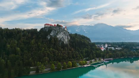 Bled-Castle-On-Rocky-Cliff-Overlooking-Lake-With-Mountains-in-Background,-Aerial-Low-Angle-Drone-Shot,-Beautiful-Travel-Destination,-Early-Morning,-Cinematic-4K