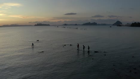 Aerial-shot-of-the-silhouette-young-boys-fishing-in-the-shallow-Andaman-sea-during-sunset,-static-shot