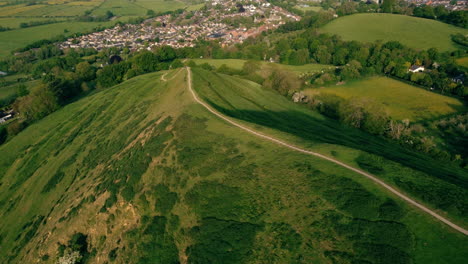A-drone-shot-descending-a-large-hill-in-Glastonbury-UK-along-a-path-towards-the-fields-below