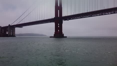 Gimbal-close-up-and-tilting-up-shot-from-a-moving-boat-as-it-approaches-the-underside-of-the-Golden-Gate-Bridge-on-a-foggy-day