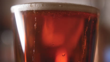 Close-up-of-beer-pouring-into-a-pint-glass-and-swirling-bubbles-rising-in-it-4K