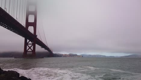 Gimbal-booming-down-shot-of-the-rocky-shoreline-at-Fort-Point-under-the-Golden-Gate-Bridge-on-a-foggy-day-in-San-Francisco,-California
