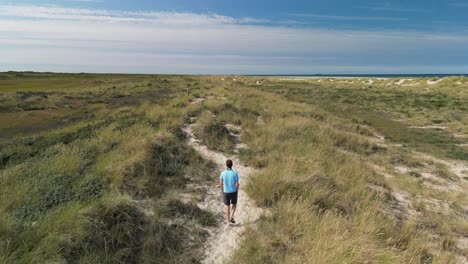 Aerial-Follow-of-Male-walking-on-sand-path-amongs-sand-dunes