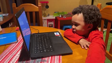 Funny-two-year-old-black-baby-plays-with-a-laptop-at-home,-seated-in-a-wooden-chair