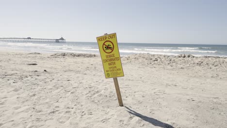 Keep-Out-Sewage-Contaminated-Water-Beware-Sign-on-Imperial-Beach-California-sunny-day---slow-motion-with-pier