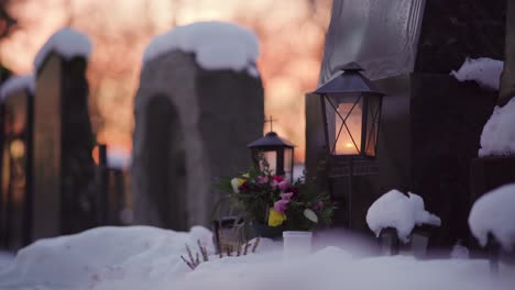 Candle-inside-a-lantern-in-front-of-a-snowy-grave-at-dusk