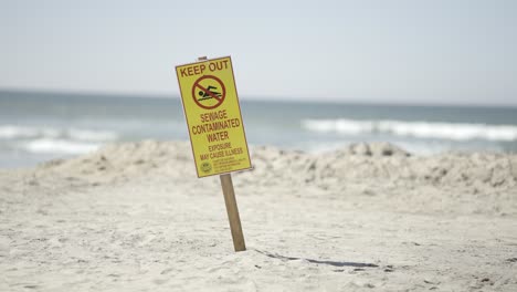 Keep-Out-Sewage-Contaminated-Water-Beware-Sign-on-Imperial-Beach-California-sunny-day---slow-motion-tight-shot