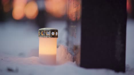 LED-candle-in-front-of-a-snowy-grave-at-dusk