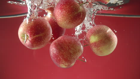 Slow-motion-of-fresh-organic-apples-falling-into-water-on-red-background