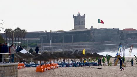 The-photographers-team-and-surfers-waiting-for-the-big-event-with-perfect-waves-and-the-best-tube-riders-in-Carcavelos-in-a-perfect-chapter-with-fort-Saint-Julian-and-portuguese-flag-in-background