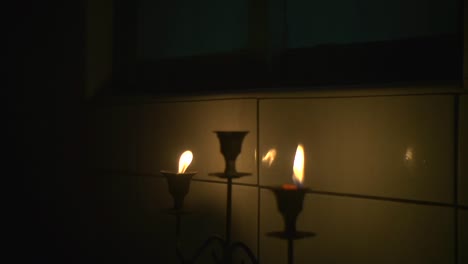 Two-candles-on-candle-holder-lit-and-placed-near-tiled-wall-for-warm-and-cozy-ethereal-feeling,-filmed-as-close-up