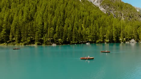 Arial-drone-shot-of-boats-rowing-in-the-river,-in-the-back-there-is-a-forest-of-pine-trees,-Lago-di-Braies,-Italy,-Dolomites