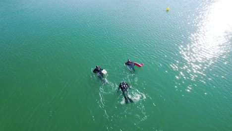 Aerial-view-of-3-divers-in-a-lake-in-southern-France,-swimming-towards-shore