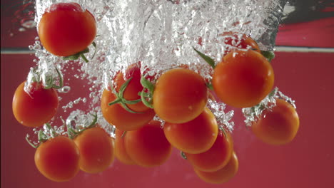 Slow-motion-of-red-cherry-tomatos-falling-into-water-on-red-background