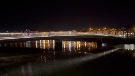 Beautifully-lit-pedestrian-bridge-over-The-river-Galao-in-Tavira-Portugal,-on-a-still-warm-spring-night