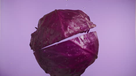 Slow-motion-of-red-cabbage-falling-into-water-surface-on-purple-background