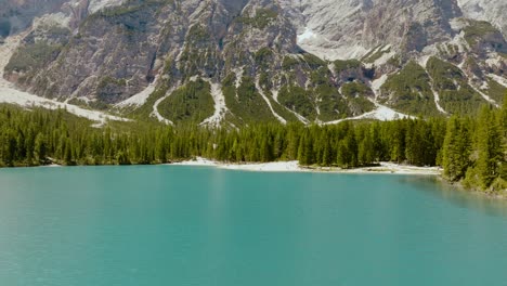 Aerial-shot-of-a-drone-above-the-river-and-the-forest-with-the-Dolomites-Alps-in-the-back,-Lago-di-Braies,-Italy,-Dolomites
