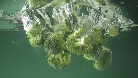 Zeitlupe-Von-Frischem,-Rohem-Brokkoli,-Der-Auf-Grünem-Hintergrund-Ins-Wasser-Fällt