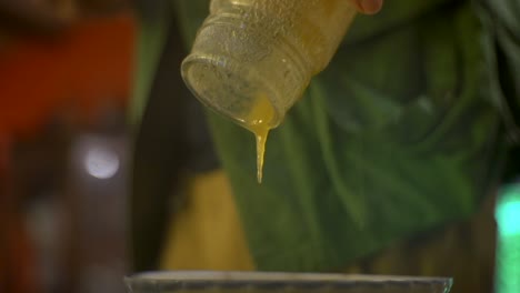 Cold-honey-in-glass-jar-slowly-oozing-into-bowl,-filmed-as-close-up-shot