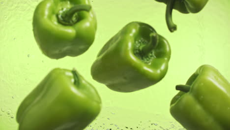 Slow-motion-of-green-peppers-falling-into-water-surface-on-green-background