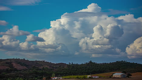 A-stack-of-cumulonimbus-clouds-forming-over-a-hillside-village---cloudscape-time-lapse