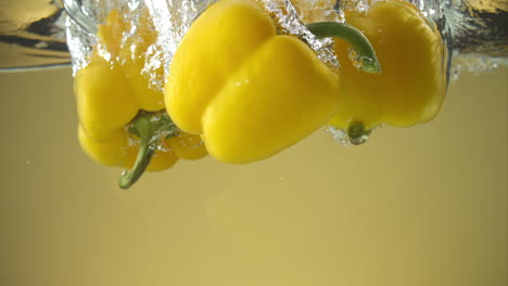 Slow-motion-of-yellow-peppers-falling-into-water-on-yellow-background