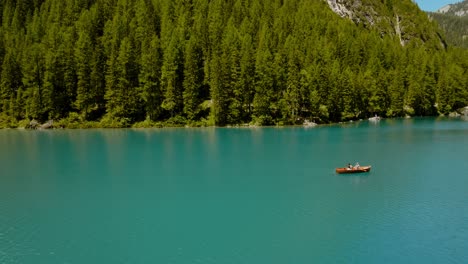 Shot-of-a-boat-rowing-in-the-river,-in-the-back-there-is-a-forest-of-pine-trees,-Lago-di-Braies,-Italy,-Dolomites
