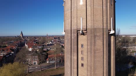 Aerial-closeup-and-reveal-of-former-Dutch-brick-water-tower-in-Zutphen-now-repurposed-as-a-residential-home-with-the-Hanseatic-town-in-the-background-against-a-blue-sky