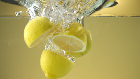 Slow-motion-of-fresh-sliced-Lemons-falling-into-water-on-yellow-background