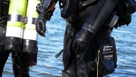 A-diver-with-his-totally-black-equipment-comes-out-of-the-water,-close-up-on-his-equipment