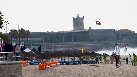 Wide-shot-of-big-event-named-"Capitulo-Perfeito"-with-the-best-tube-riders-in-Carcavelos-beach-with-fort-Saint-Julian-behind