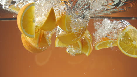 Zeitlupe-Von-Frisch-Geschnittenen-Orangen,-Die-Auf-Orangefarbenem-Hintergrund-Ins-Wasser-Fallen