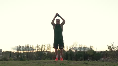 A-muscular-sportsman-does-broad-jumps-in-a-park,-with-the-sunset-behind