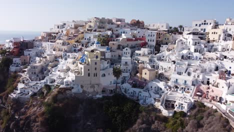 Aerial:-Slow-panning-drone-shot-of-Oia-in-Santorini,-Greece-during-golden-hour