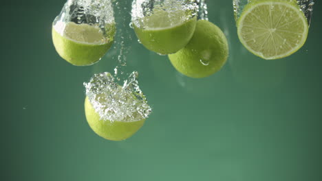 Slow-motion-of-fresh-sliced-Limes-falling-into-water-on-green-background