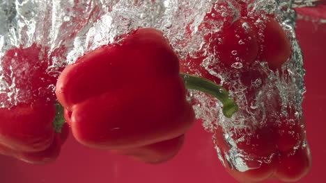 Slow-motion-of-red-peppers-falling-into-water-on-red-background