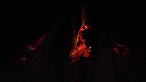 Embers-of-coal-glowing-red-hot-with-small-flames-burning-in-wood-fire,-filmed-as-close-up-in-slow-motion