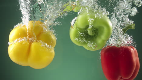 Slow-motion-of-Colorful-peppers-falling-into-water-on-green-background