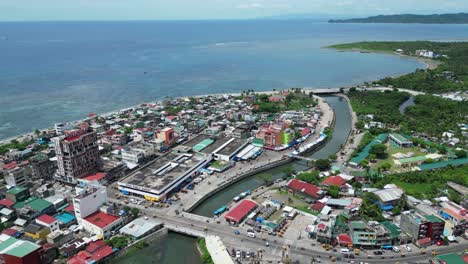 High-Angle,-Rising,-Aerial-View-of-Waterfront-town-of-Virac,-Catanduanes,-Philippines-with-busy-traffic-and-open-Sea-in-background