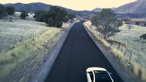 cinematic-blue-hour-car-chase-in-snow-basin-Utah-white-car-driving-fast-down-a-mountain-valley-road---AERIAL-CHASE-FOLLOW