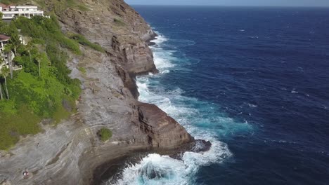 reveal-shot-of-bright-greenery-and-massive-waves-crashing-in-tropical-spitting-cave-in-honolulu-hawaii---AERIAL-PULLBACK-REVEAL