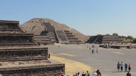 Wide-panning-shot-of-the-archaeological-site-of-Teotihuacan-in-Mexico,-with-the-Pyramid-of-the-Moon-and-other-ruins-and-people-walking-around-on-a-clear-and-sunny-day