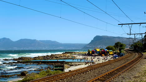St-James-beach-with-colorful-bathing-boxes-next-to-railroad,-Muizenberg