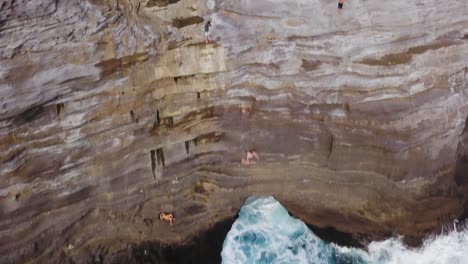 young-man-cliff-jumping-into-spitting-cave-honolulu-hawaii-while-people-watch---AERIAL-PULLBACK