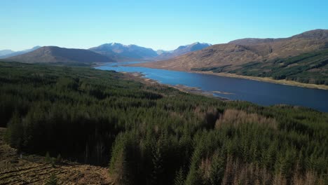 Rise-over-pine-forest-treeline-revealing-dark-lake-of-Loch-Loyne-Scottish-Highlands