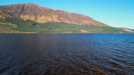 Vuelo-Lento-Y-Bajo-Sobre-Loch-Lochy-Hacia-Montañas-Iluminadas-Por-El-Sol-En-Las-Tierras-Altas-Escocesas