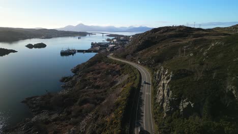 Flying-along-road-to-Kyle-of-Lochalsh-with-traffic-an-pan-up-revealing-Skye-bridge-and-Cuillin-mountains-in-Scottish-Highlands