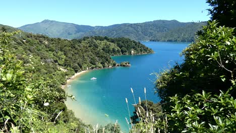 Kayakers-are-framed-from-a-high-vantage-point-as-they-paddle-into-secluded-bay-on-turquoise-water-in-summertime---Governors-Bay,-Marlborough-Sounds