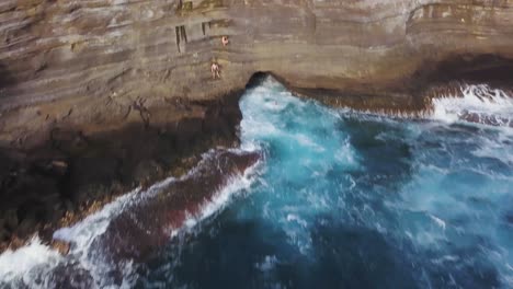 young-man-cliff-jumping-off-spitting-cave-in-honolulu-hawai-with-bright-blue-ocean-water---AERIAL-DOLLY-BACK-TILT