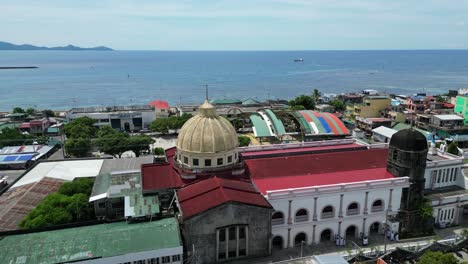 Vista-Aérea-Giratoria-De-La-Antigua-Iglesia-Catedral-En-El-Centro-De-Virac,-Catanduanes-Con-Mar-Turquesa-En-El-Fondo